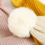 Primo piano di un grande pompon bianco tra berretti a coste con pompon nei colori rosa, giallo e beige