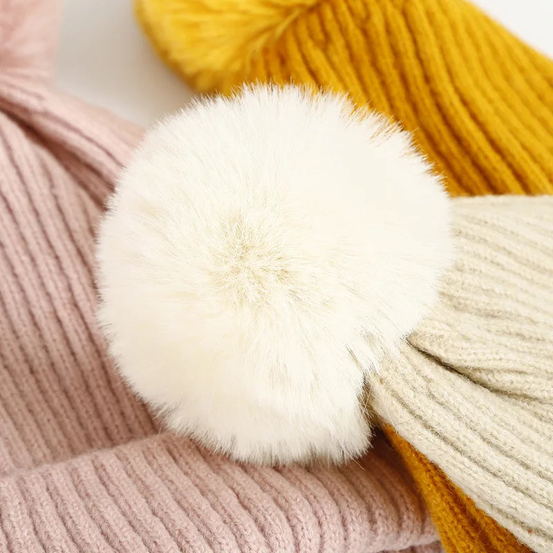 Primo piano di un grande pompon bianco tra berretti a coste con pompon nei colori rosa, giallo e beige