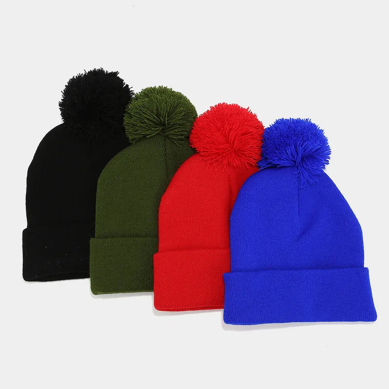 Quattro berretti con pompon e risvolto, nero, verde oliva, rosso e blu, disposti uno accanto all’altro