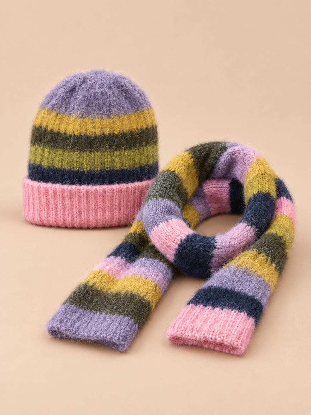 Set berretto e sciarpa con righe arcobaleno su fondo rosa e pezzi coordinati nei colori, vista frontale