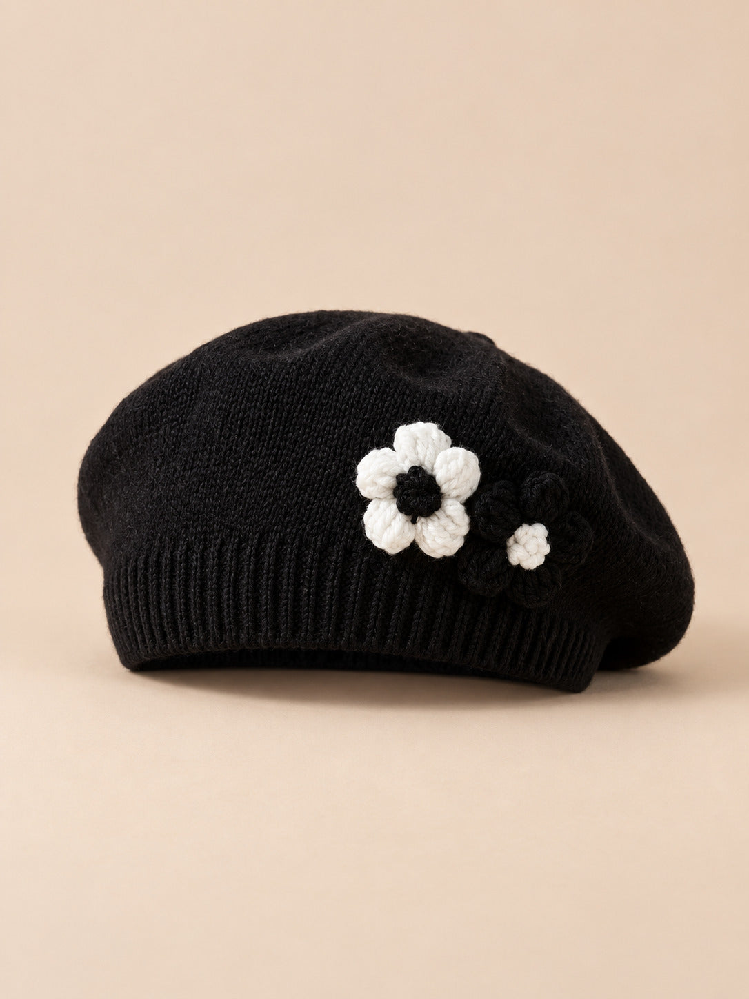 Basco nero da bambina con fiori in rilievo lavorati a maglia, su sfondo color sabbia e pesca