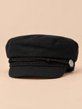 Cappello da marinaio nero a otto spicchi con visiera, stile capitano, su sfondo color sabbia e pesca