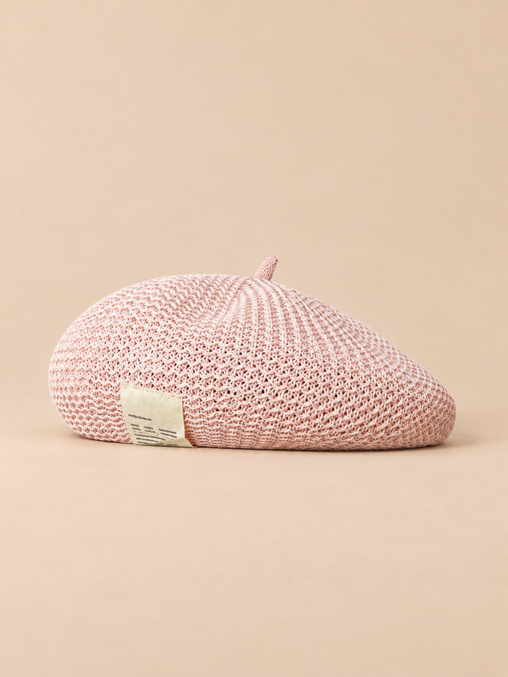 Basco estivo rosa da donna effetto paglia, leggero e traforato, su sfondo color sabbia e pesca