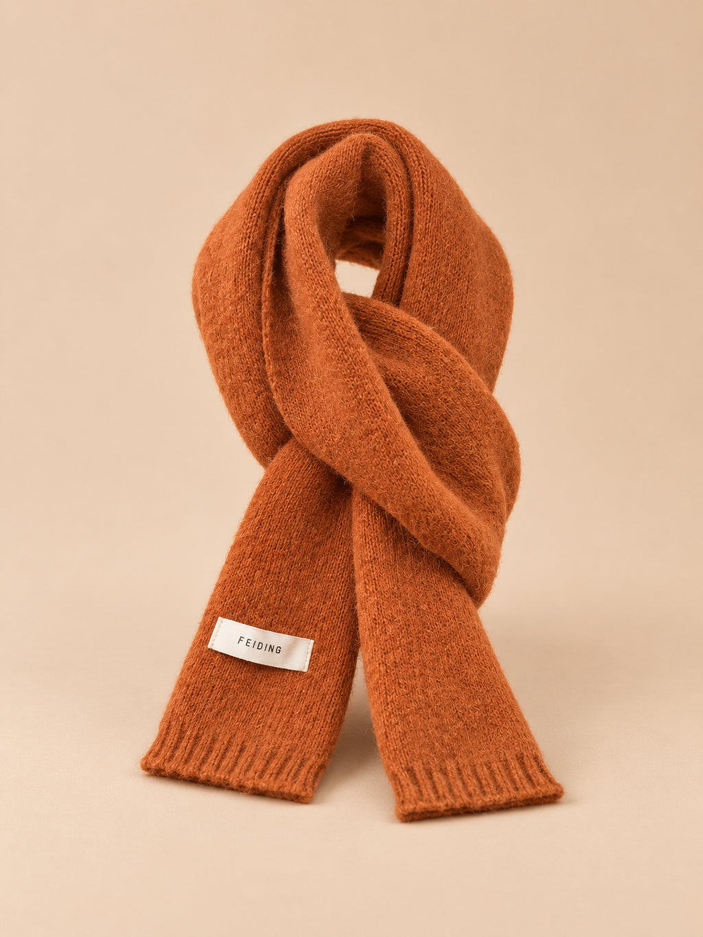 Sciarpa classica arancione in maglia a tinta unita per l’inverno, su sfondo color sabbia e pesca