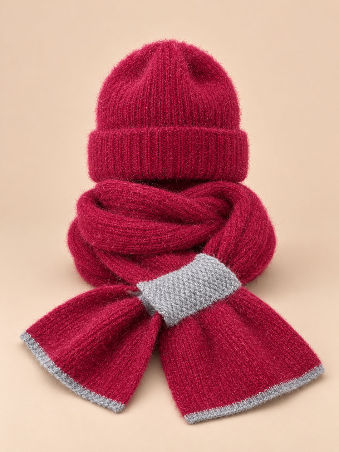 Set berretto e sciarpa da donna bordeaux in maglia effetto peluche, su sfondo color sabbia e pesca
