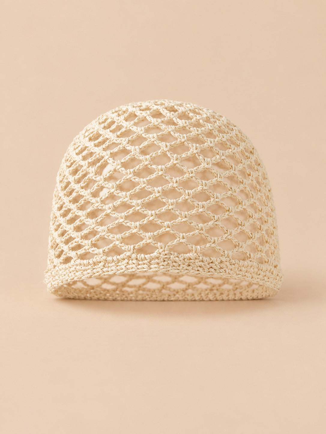 Cappello estivo leggero da donna in rete di cotone beige, visto di fronte su sfondo sabbia e pesca